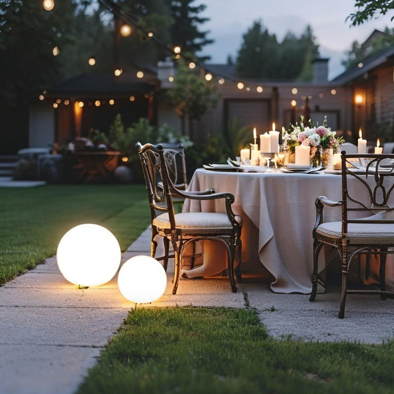 Outdoor dinner setup with string lights and illuminated spherical lamps in a backyard.