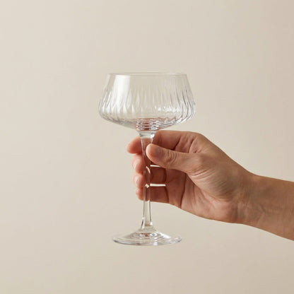 Hand holding a clear glass wine glass against a beige background