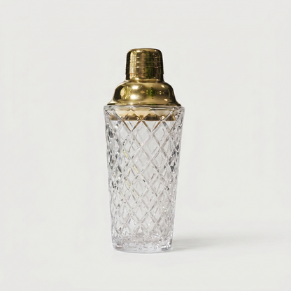 Glass cocktail shaker with gold lid on white background
