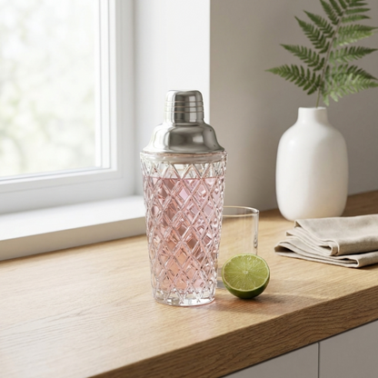 Glass cocktail shaker with copper lid on white counter beside lime