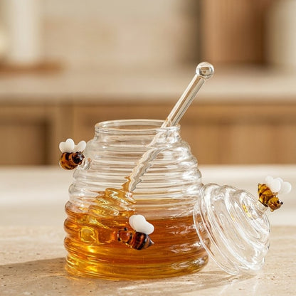 Beehive-shaped glass honey jar open on a kitchen counter with the lid and dipper set beside it