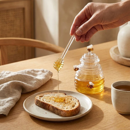 Hand drizzling honey from the dipper onto buttered toast beside the beehive glass jar