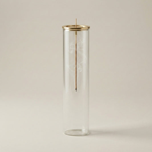 Clear glass cylinder incense burner with gold accent on a beige background