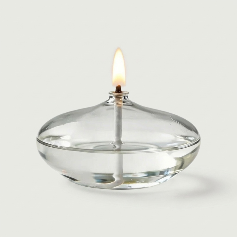 Glass oil candle on white background with lit flame