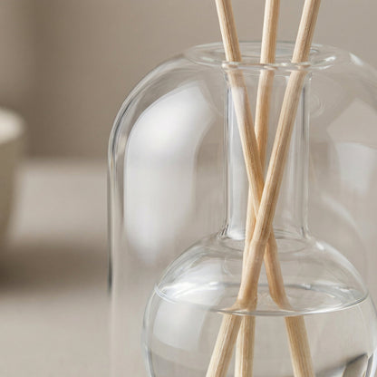 Clear glass diffuser bottle with wooden sticks on a neutral background