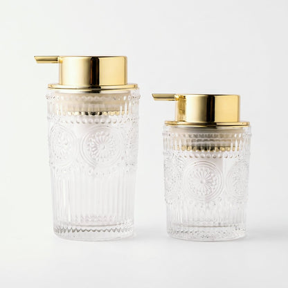 Medium and small clear glass soap dispensers with gold pumps side by side on a light background