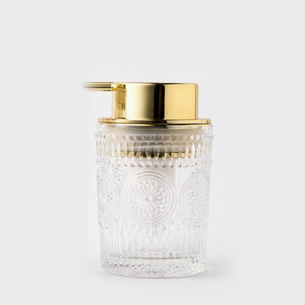 Small clear embossed glass soap dispenser with a gold pump on a light grey background