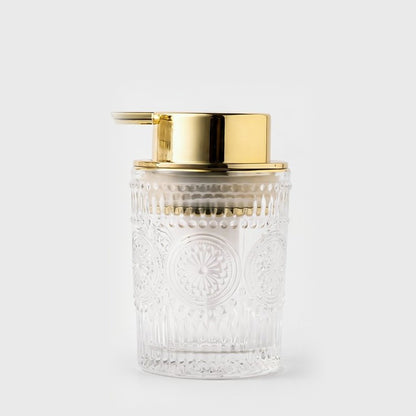 Small clear embossed glass soap dispenser with a gold pump on a light grey background