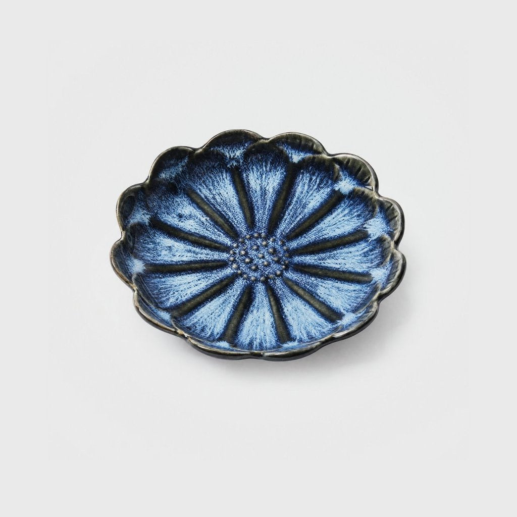 Single cobalt blue glazed ceramic dish with white feathering, a scalloped rim and a daisy-like petal pattern on a plain light gray background
