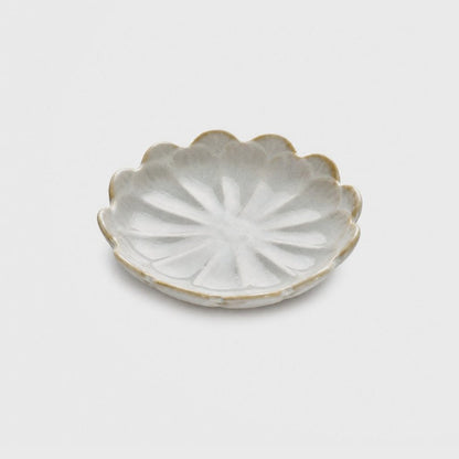 Single glossy off-white to pale gray glazed ceramic dish with a scalloped petal-lobed rim and tan edges on a plain light gray background