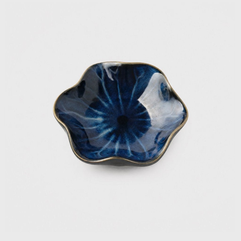 Single glossy deep navy glazed ceramic dish with pale blue streaks and a thin bronze rim in a wavy flower shape on a plain light gray background