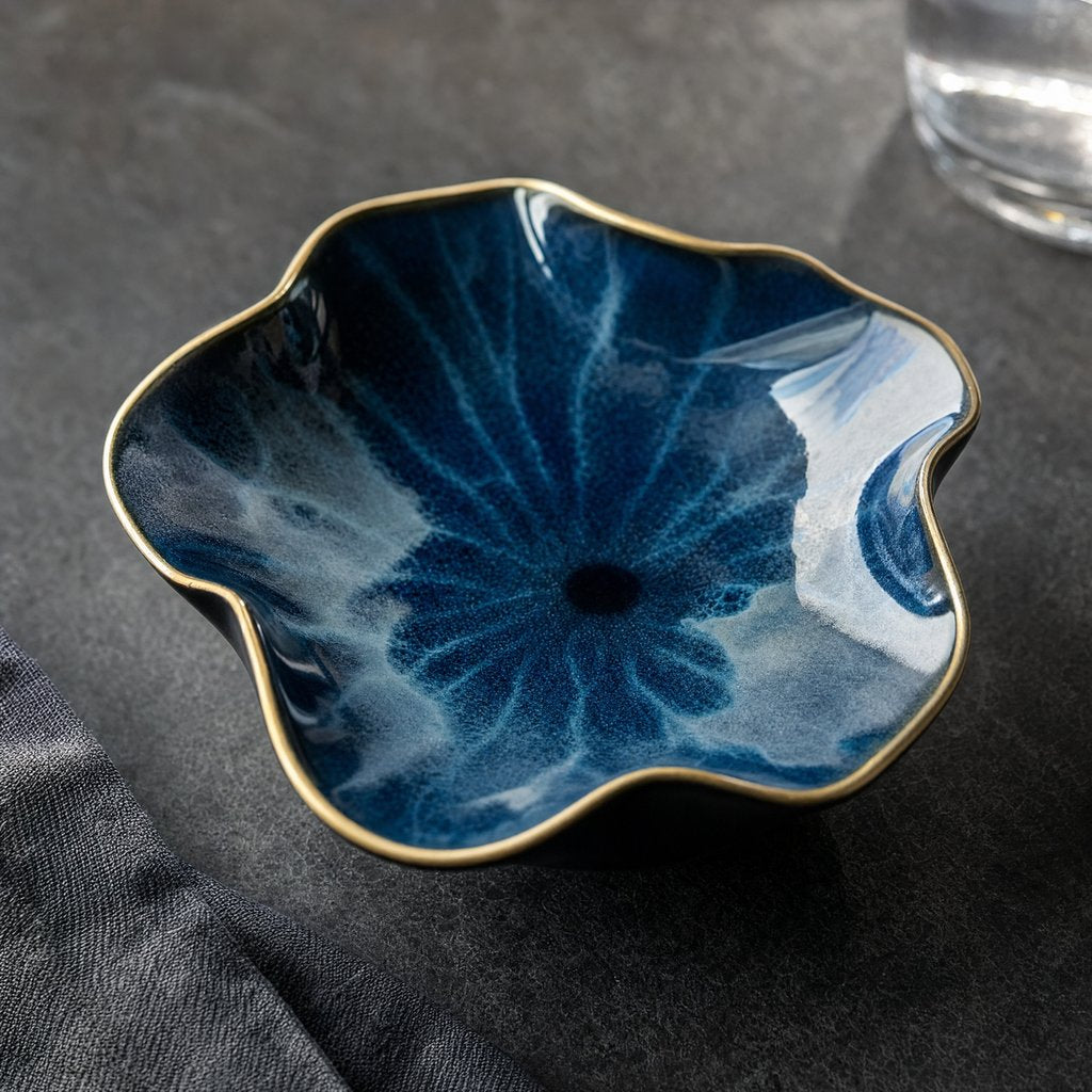 Empty deep navy glazed ceramic dish with white marbled swirls and a thin gold rim on a dark gray slate surface with a folded gray linen cloth