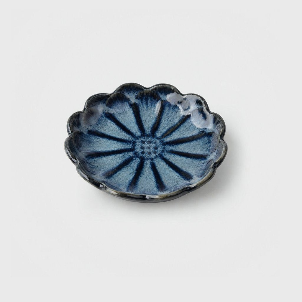 Single steel-blue glazed ceramic dish with a dark navy scalloped rim and a daisy-like petal pattern on a plain light gray background