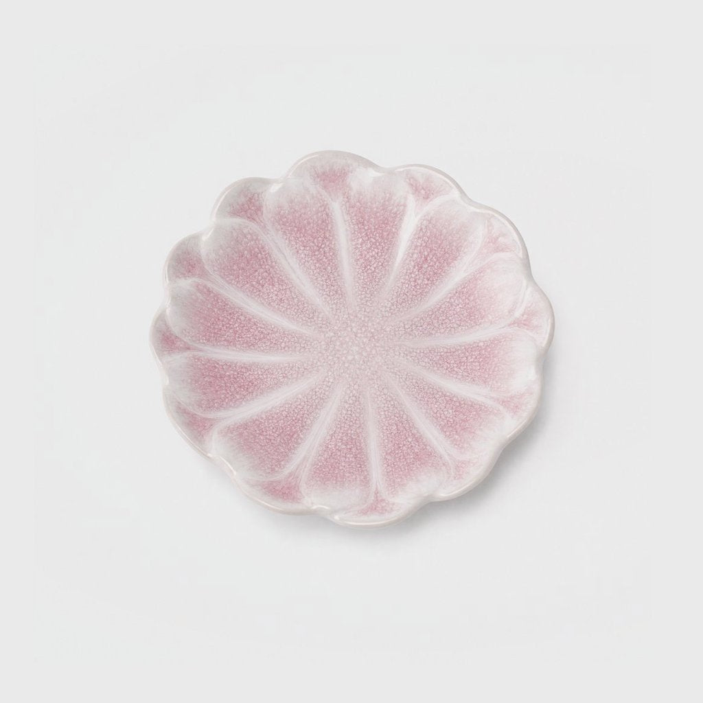 Overhead view of a single soft pink glazed ceramic dish with a scalloped flower-shaped rim and raised petal ridges on a plain light gray background