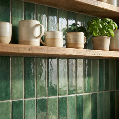 Forest green glossy subway tile behind open wood shelving with ceramic mugs and a potted basil plant