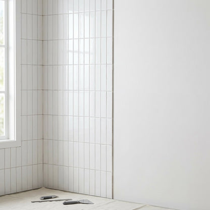 White glossy subway tile partially installed on a wall corner with a utility knife and trowel on a drop cloth