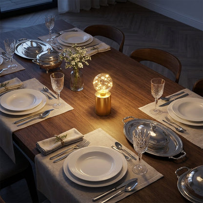 Lit glass globe LED lamp on a formally set dining table with crystal wine glasses and silver serving dishes