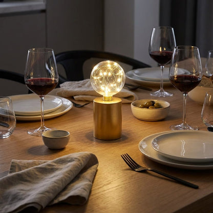 Lit glass globe LED lamp centered among stemmed wine glasses and a bowl of olives on a dining table