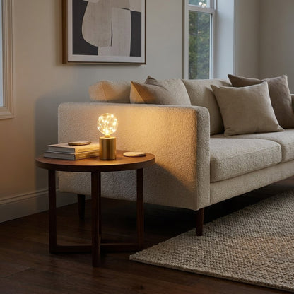 Lit glass globe LED lamp on a round wood side table beside a boucle sofa with a stack of books