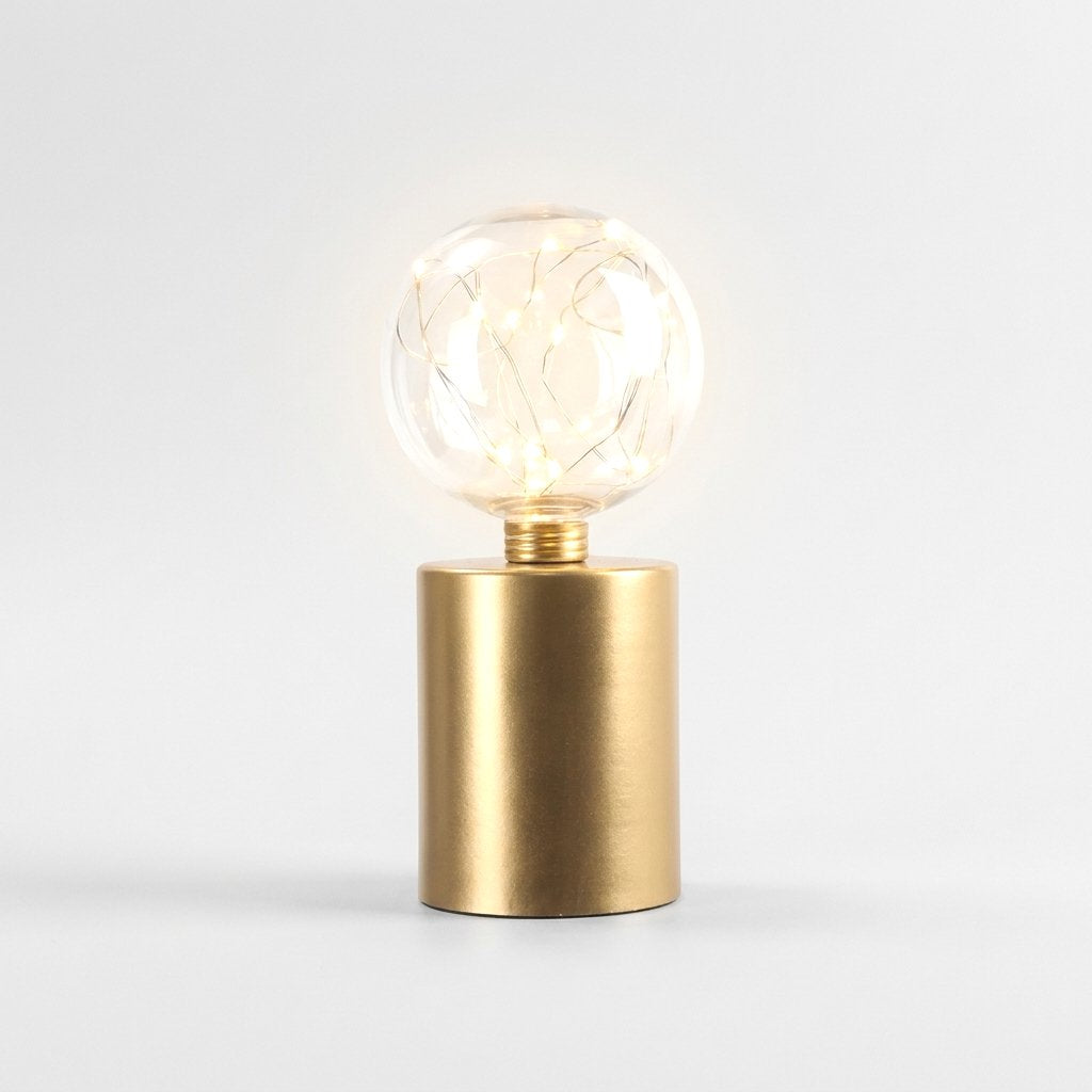 Single lit clear glass globe LED lamp on a brass base, on a plain studio background