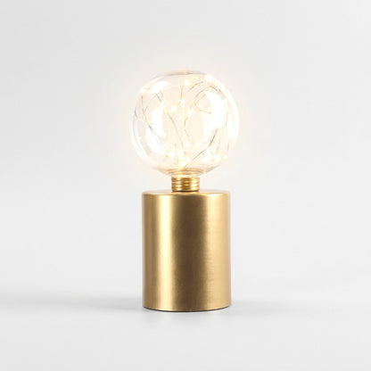 Single lit clear glass globe LED lamp on a brass base, on a plain studio background