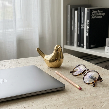 Gold bird sculpture on white desk beside notebook and glasses