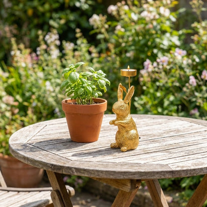 Gold standing rabbit candle holder on outdoor garden table beside potted basil