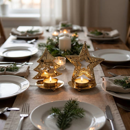 Gold-plated tree-shaped and star-shaped tealight candle holders with lit candles on a formally set dining table with greenery and folded napkins