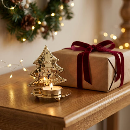 Gold-plated tree-shaped tealight candle holder with a lit candle on a console table beside a wrapped gift and pine wreath