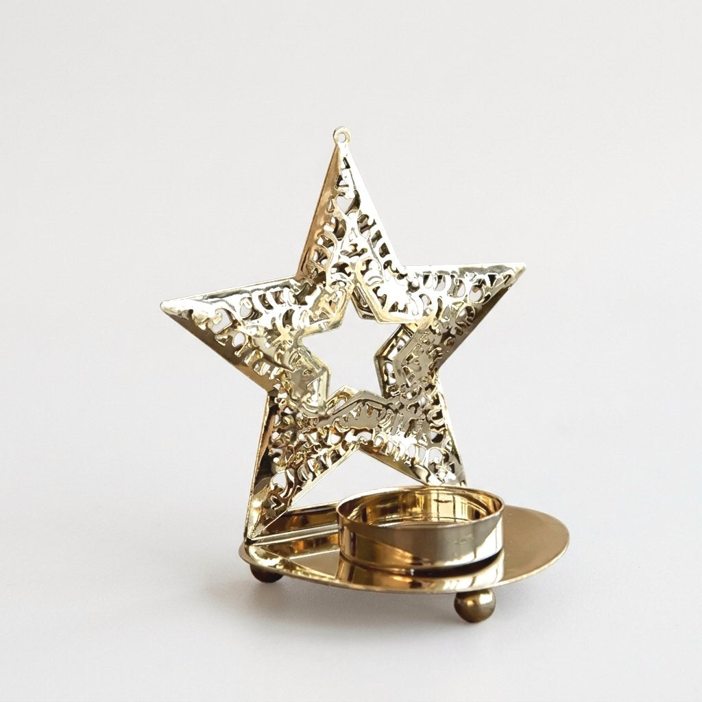 Gold-plated star-shaped tealight candle holder with an unlit candle on a plain background