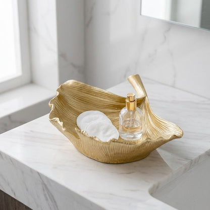 Gold ginkgo leaf tray holding cotton rounds and a perfume bottle on a marble bathroom vanity