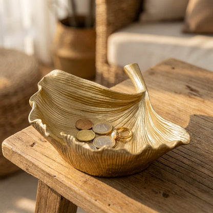 Gold ginkgo leaf tray holding coins and a ring on an outdoor side table