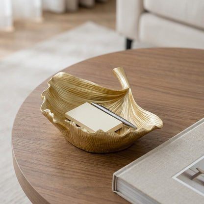 Gold ginkgo leaf tray holding a notepad and pen on a round side table