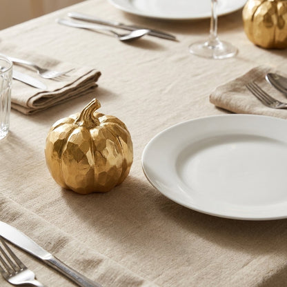 Gold faceted pumpkins on a linen-dressed dining table set with two full place settings