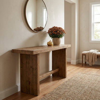 Gold faceted pumpkin on an entryway console table beside a potted orange mum, below a round mirror