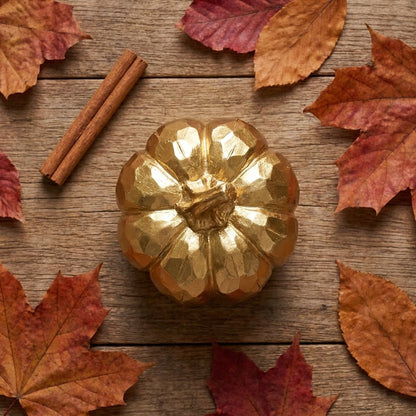 Overhead view of a gold faceted pumpkin surrounded by scattered maple leaves and cinnamon sticks on a wood surface