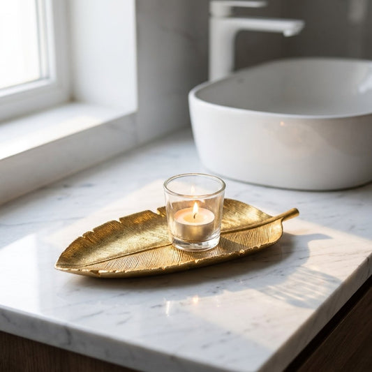 Gold leaf tray holding a lit tealight candle on a white marble bathroom counter