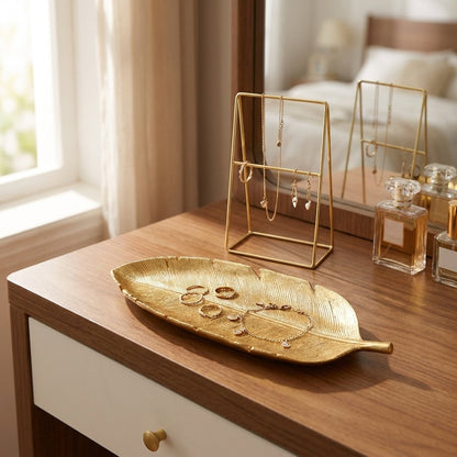 Gold leaf tray with rings and a bracelet on a vanity beside a jewelry stand