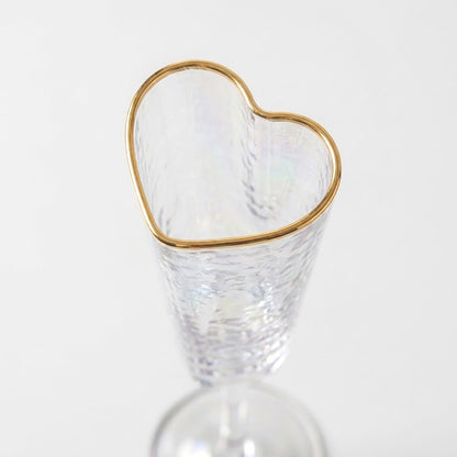 Close-up of a heart-shaped champagne flute rim traced in gold with hammered glass texture