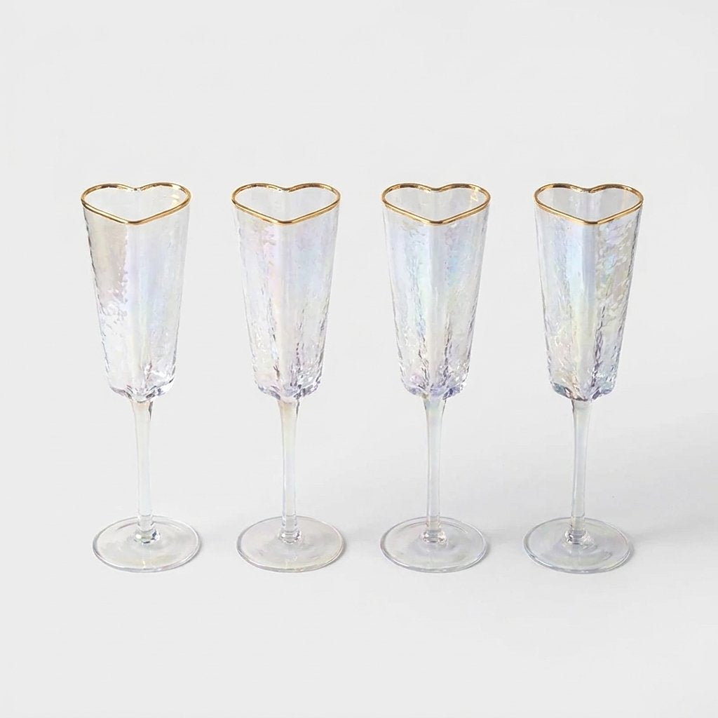 Set of four empty gold-rim heart champagne flutes lined up on a white background