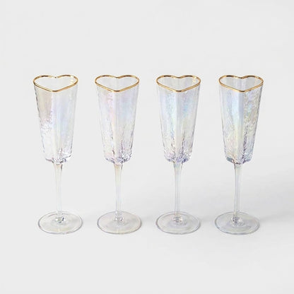 Set of four empty gold-rim heart champagne flutes lined up on a white background