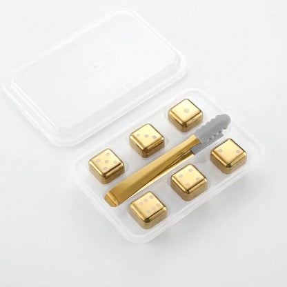Six gold dice-style chilling stones with dot faces in a clear tray with gold tongs on a white background