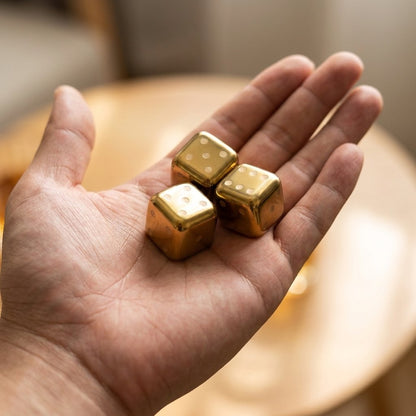 Open hand holding three gold dice-style chilling stones with dot faces