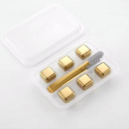 Six plain gold chilling stones in a clear tray with gold tongs on a white background