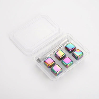 Six iridescent rainbow chilling stones in a clear tray with silver tongs on a white background