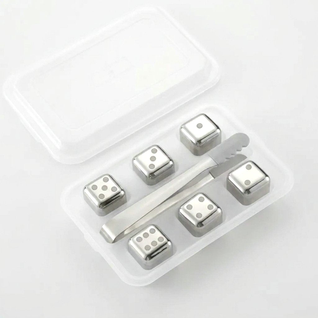 Six silver dice-style chilling stones with dot faces in a clear tray with silver tongs on a white background