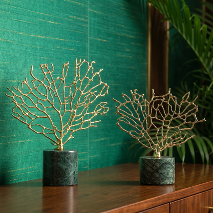 Two gold leafed decorative pieces in green pots on a wooden surface with a teal textured wall in the background.