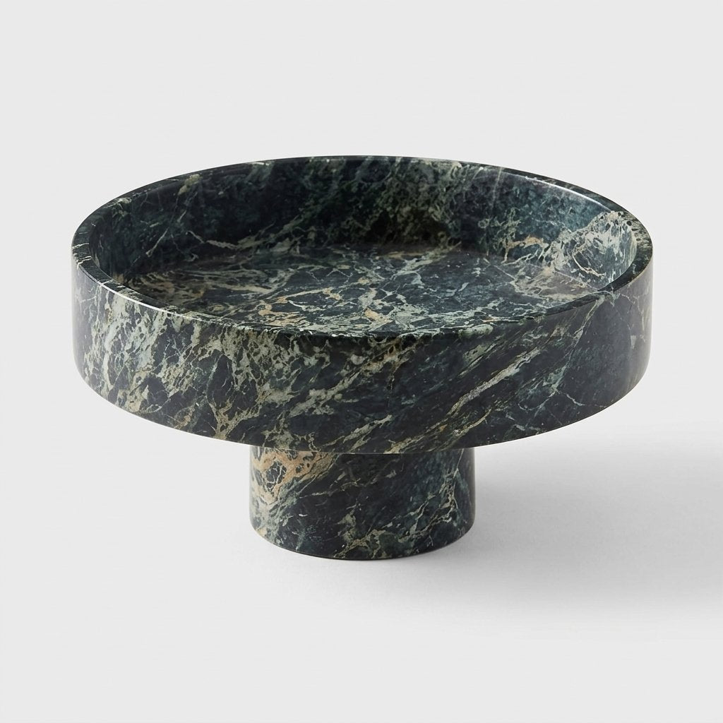 Empty green marble pedestal fruit bowl with natural veining, shown at an angle on a plain studio background