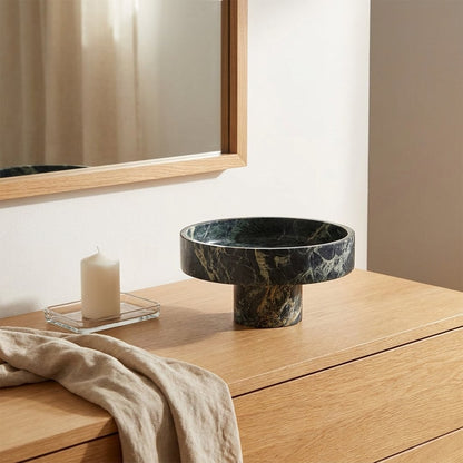 Empty green marble pedestal fruit bowl on a wood dresser beneath a mirror, beside a lit candle