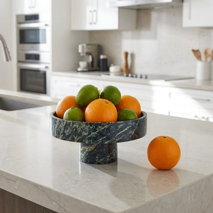 Green marble pedestal fruit bowl filled with oranges and limes on a white stone kitchen counter